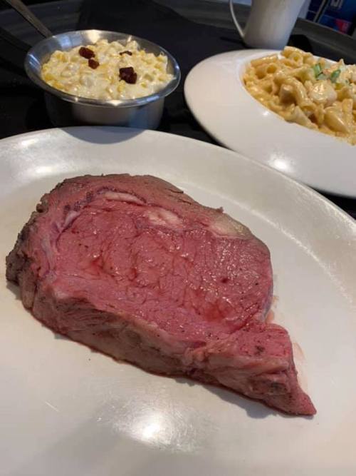 A plate featuring a juicy prime rib, a bowl of creamy macaroni, and a side of corn salad.