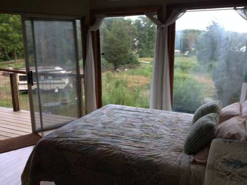 Cozy bedroom with a quilted bedspread and large windows overlooking a green landscape.