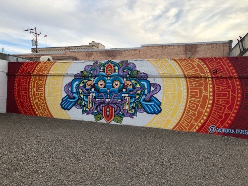 Colorful mural featuring a stylized blue creature with intricate patterns and symbols against a vibrant background.