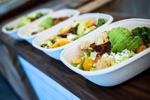 Four salad bowls with various fresh ingredients, including greens, fruits, and toppings, arranged on a wooden surface.