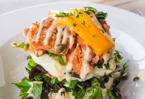 A colorful salad topped with grilled salmon, mango slices, and drizzled with creamy dressing on a bed of greens.
