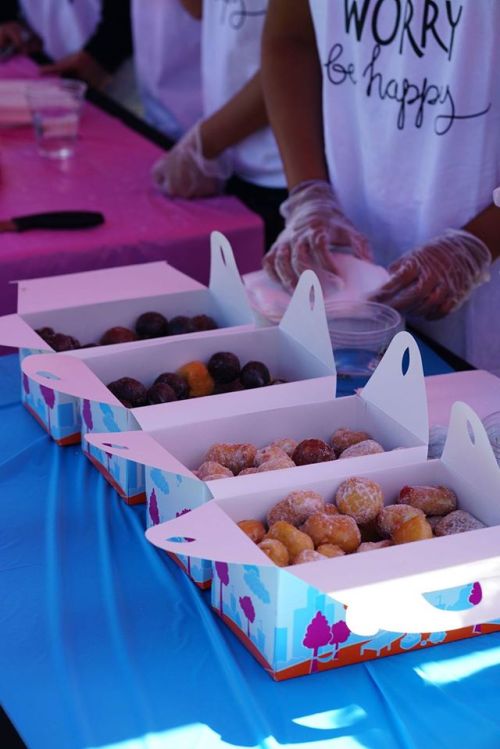 Boxes of assorted donuts on a table, with people in the background wearing gloves and t-shirts.