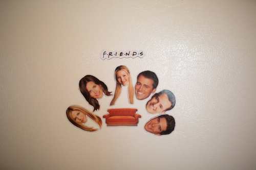 Colorful cutouts of six characters from "Friends" arranged around a central orange couch, with the show's title above.
