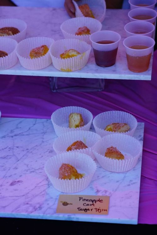 A display of pineapple-flavored treats in paper cups, with small cups of drink in the background on a marble surface.