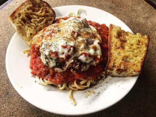 A plate of pasta topped with marinara sauce, melted cheese, and two slices of toasted bread on the side.