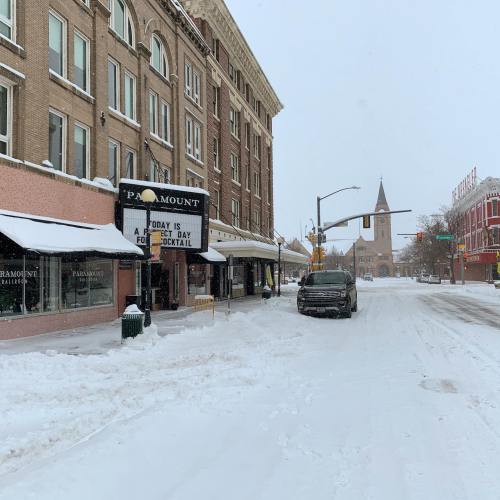 Snow-covered street scene featuring a theater marquee and a truck, with buildings and a church in the background.