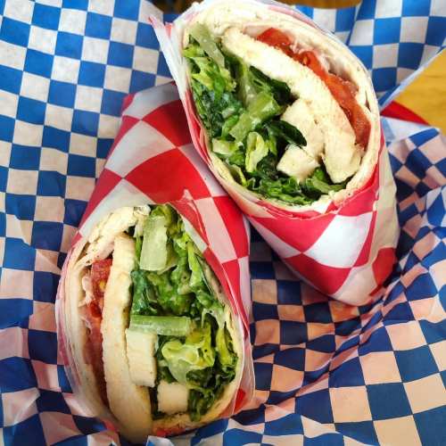 Two wrapped sandwiches with chicken, lettuce, and tomato, served in a red and white checkered paper basket.
