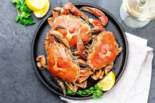 A black plate with two cooked crabs, garnished with lemon wedges and fresh cilantro, on a gray surface.