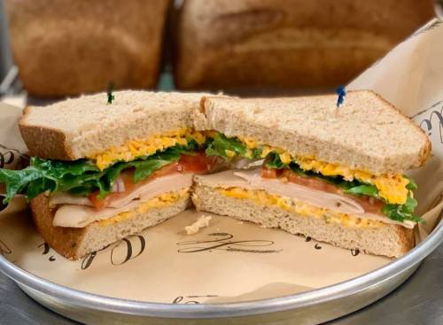A freshly cut sandwich with turkey, lettuce, tomato, and cheddar cheese on whole grain bread, served on a plate.