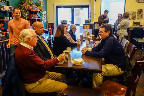 A group of people seated at a table in a café, engaged in conversation with coffee cups in front of them.