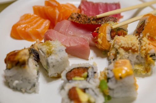 A plate of assorted sushi, including salmon, tuna, and various rolls, with chopsticks resting on top.