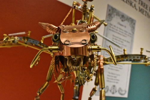 A detailed metallic sculpture of a creature with horns, made from copper and various mechanical parts.