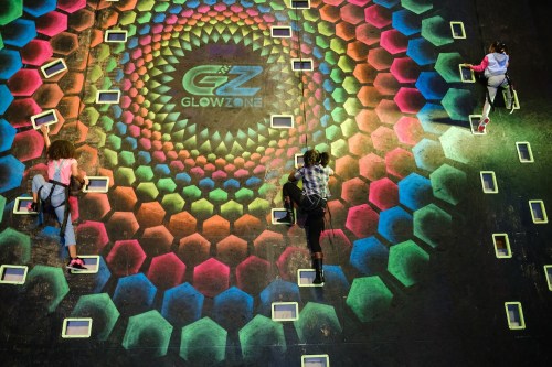 Three climbers ascend a colorful, hexagonal-patterned wall at GlowZone, with a vibrant design beneath them.