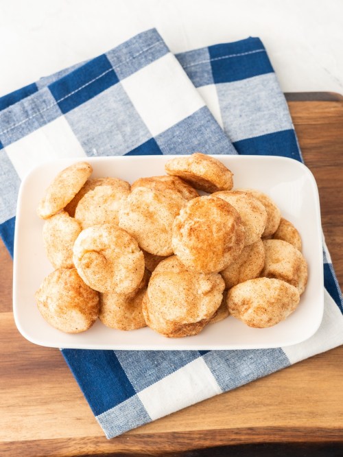 A white dish filled with round, cinnamon-sugar coated cookies on a blue and white checkered cloth.