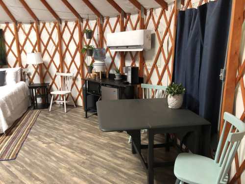 Interior of a cozy yurt featuring a table, chairs, kitchenette, and wooden walls with a rustic design.