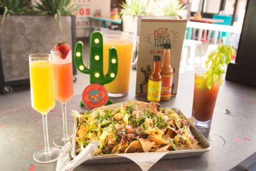 A vibrant table setting with nachos topped with greens, two colorful drinks, and a cactus decoration.