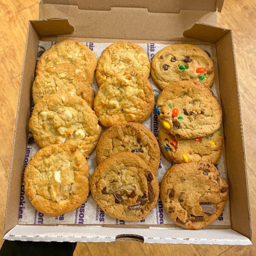 A box of assorted cookies, featuring chocolate chip, M&M, and white chocolate varieties, neatly arranged.