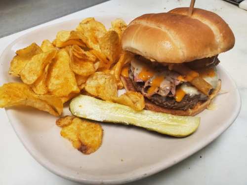 A juicy burger with melted cheese, topped with crispy onions, served with potato chips and a pickle on the side.