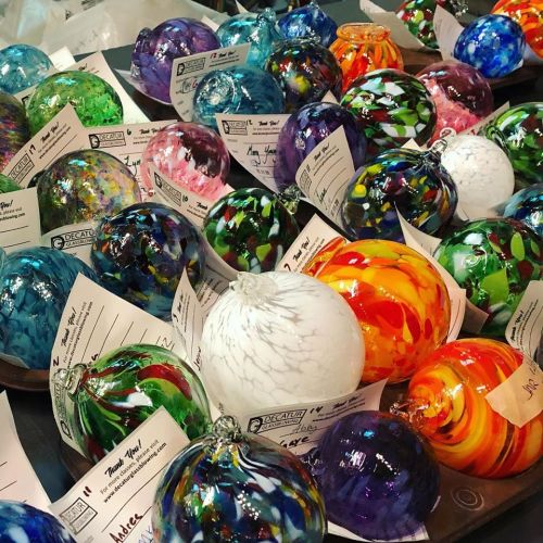A colorful assortment of glass ornaments in various patterns and colors, displayed with tags on a table.