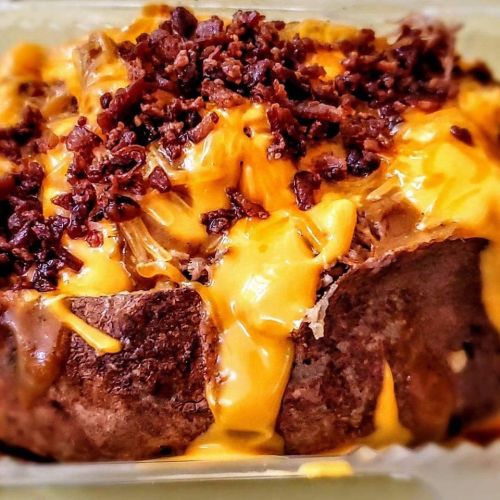 A close-up of a cheesy meatloaf topped with crispy bacon bits, served in a dish.