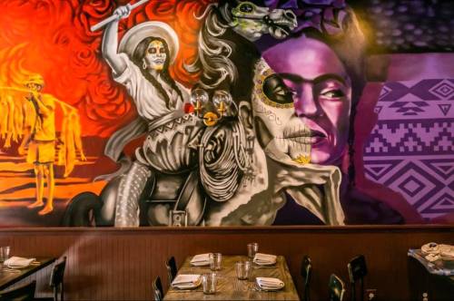 Colorful mural featuring a woman on a horse, skull motifs, and vibrant patterns, set in a restaurant interior.