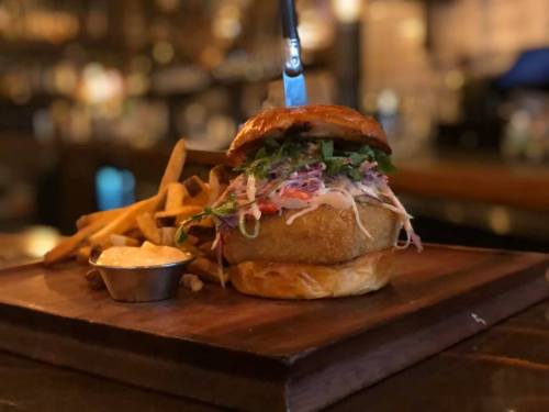 A gourmet burger topped with slaw, served with fries and dipping sauce on a wooden platter.