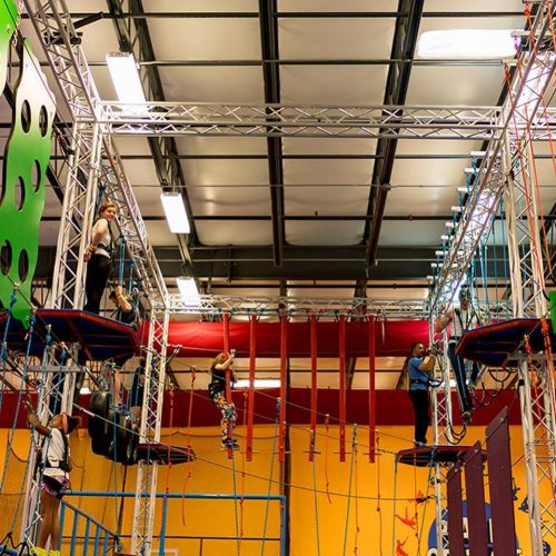 Indoor climbing facility with multiple levels, featuring climbers on ropes and various climbing structures.