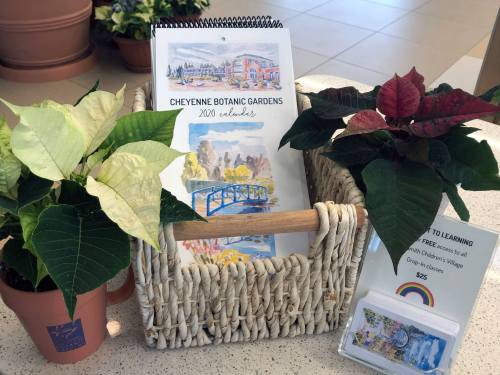 A woven basket holds a 2020 calendar of Cheyenne Botanic Gardens, surrounded by potted poinsettias and a sign for free classes.