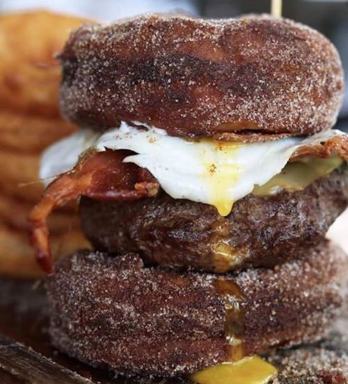 A stacked burger with bacon and a fried egg, sandwiched between two sugared donuts.