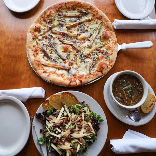 A table setting with a pizza topped with green beans, a salad with nuts and cheese, and a bowl of soup.