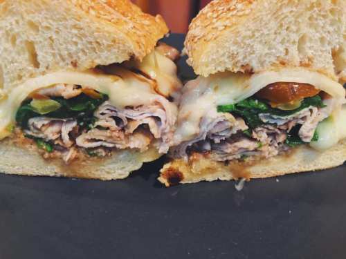 Close-up of a sliced sandwich with turkey, spinach, melted cheese, and a savory sauce on sesame seed bread.