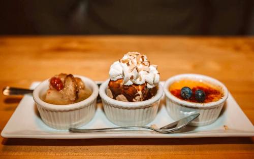 A dessert trio featuring a fruit compote, a sundae with whipped cream and nuts, and a crème brûlée with blueberries.