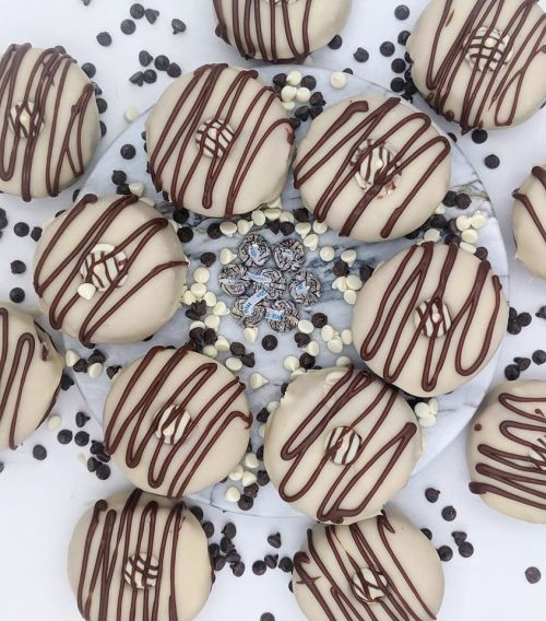 A plate of round cookies drizzled with chocolate, surrounded by chocolate chips and white chocolate pieces.