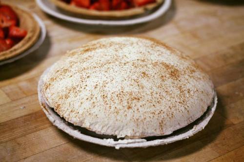 A round, fluffy meringue pie topped with a dusting of cinnamon, resting on a wooden surface.