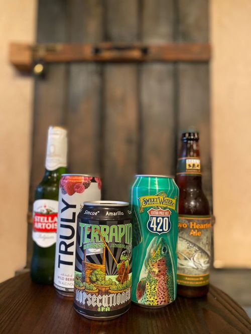 A selection of craft beers and hard seltzer on a wooden table, with a rustic background.
