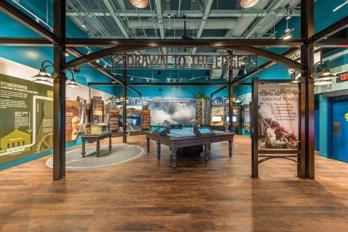 Exhibit space featuring informational displays, a central table, and a blue wall backdrop in a museum setting.
