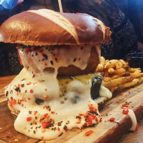 A towering burger with melted cheese, a pretzel bun, and colorful sprinkles, served with fries on a wooden platter.