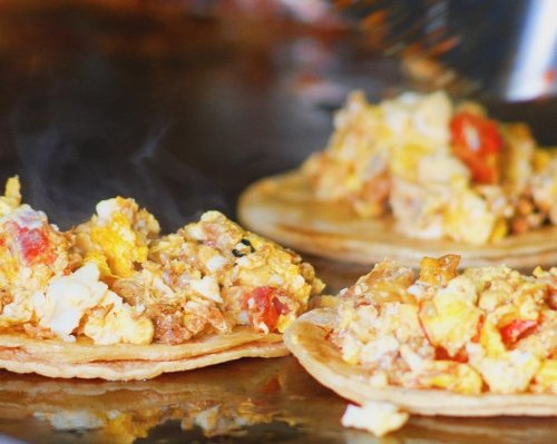 Three tortillas filled with scrambled eggs, tomatoes, and spices, steaming on a hot griddle.