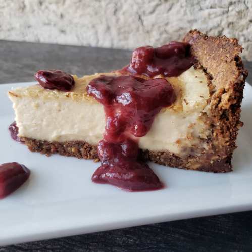 A slice of cheesecake topped with cherry sauce on a white plate, set against a textured background.