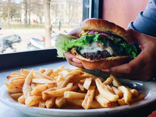 A hand holds a juicy burger with lettuce and cheese, accompanied by a plate of golden French fries.