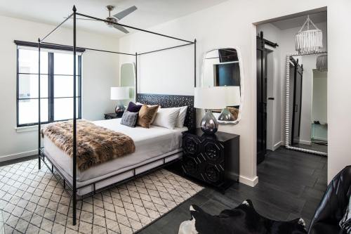 A modern bedroom featuring a four-poster bed, stylish decor, and a large mirror, with natural light streaming in.