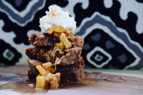 A stack of dessert topped with whipped cream and caramelized apples, set against a patterned background.