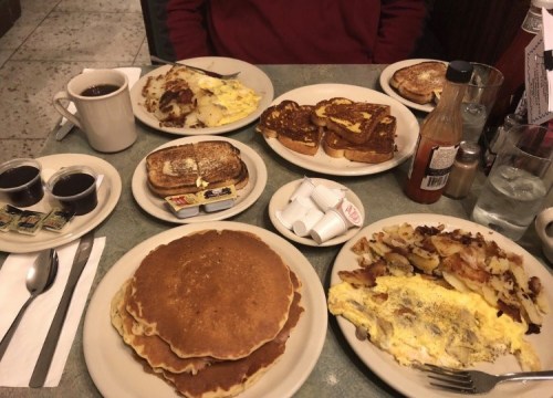 A table filled with breakfast items: pancakes, eggs, French toast, hash browns, coffee, and syrup.
