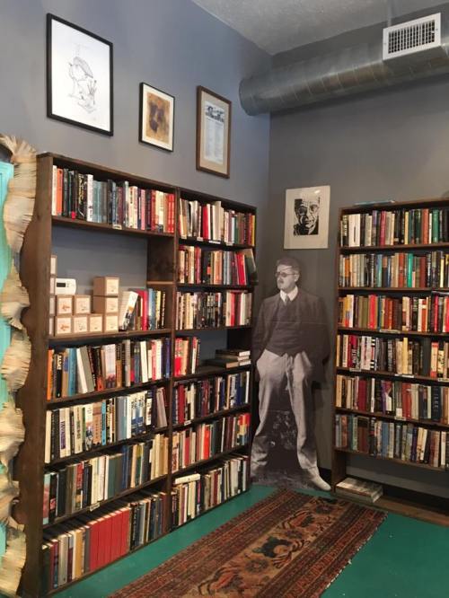 A cozy room filled with bookshelves, featuring a life-sized cutout of a man in a suit standing among the books.