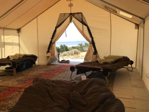 Interior of a tent with two cots, a rug, and an open entrance showing a view of the outdoors.