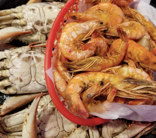 A red basket filled with cooked shrimp, placed on a bed of crab shells.