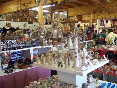 A display of various handcrafted figurines and souvenirs in a rustic shop, with wooden decor and customers browsing.