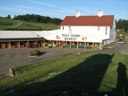 A large market building with a red roof, surrounded by greenery and a tractor in front, at Trax Farms.