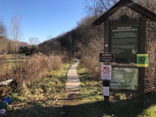 A wooden path leads into a conservation area, with signs about rules and warnings in a natural setting.