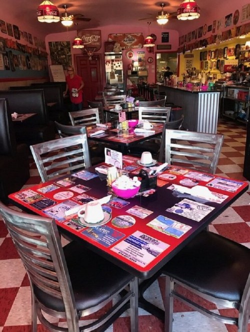 A colorful diner interior with red and white checkered floors, tables adorned with menus, and vintage decor on the walls.
